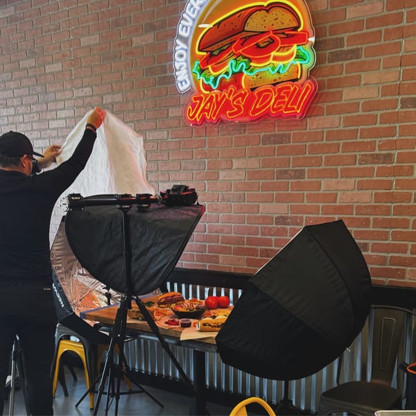 A person arranging lighting for a food photoshoot of various deli items at Jay's Deli.